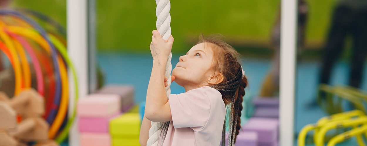 Ein Kind klettert im Kinderturnen ein Seil hoch